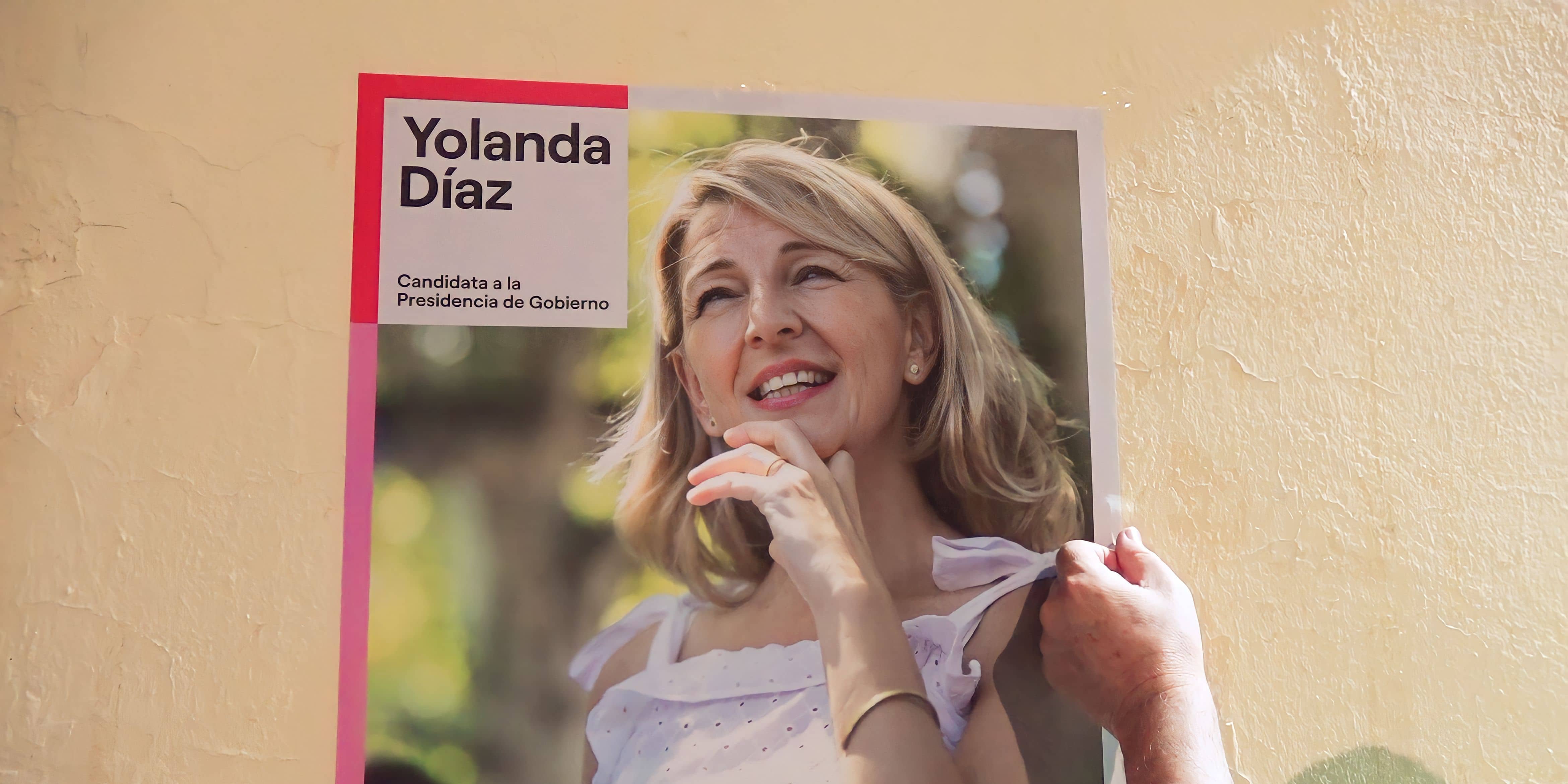 Paco Algaba termina de colocar un cartel electoral de Yolanda Díaz, en la puerta de la sede de IU El Viso.